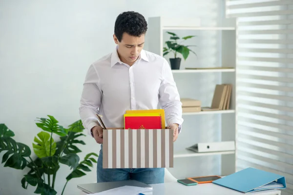 Verstoorde jonge brunette man holding box met zijn persoonlijke spullen — Stockfoto