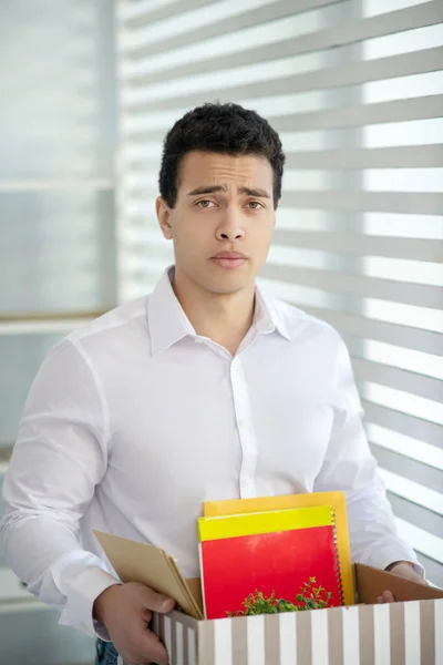 Disappointed young brunette male carrying box with his personal stuff