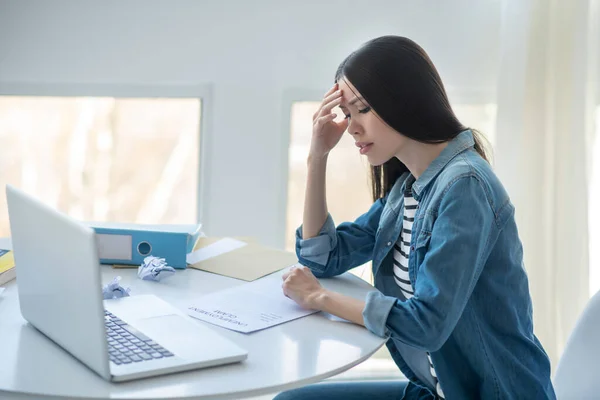 Triste femme brune assise à son bureau avec demande de prestations de chômage, touchant son nez pont — Photo