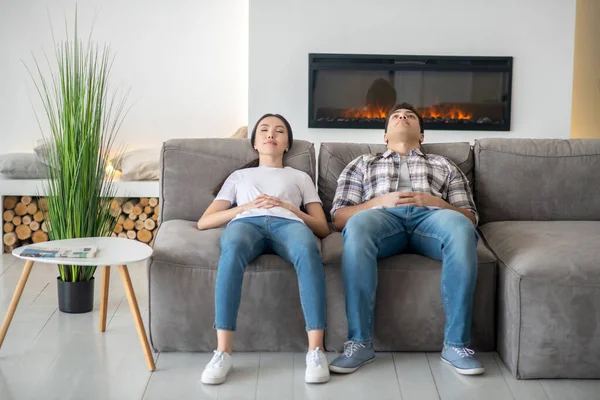 Dark-haired female and brunette male resting on sofa with closed eyes — Stock Photo, Image