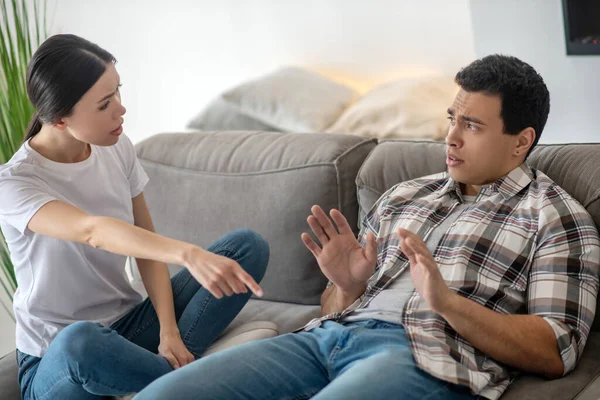 Brünetten Mann und dunkelhaarige Frau sitzen auf dem Sofa und streiten über etwas — Stockfoto