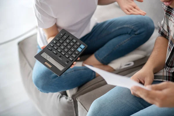 Крупним планом чоловічі руки з паперами, жіночі руки тримають калькулятор, обидва сидять на дивані — стокове фото