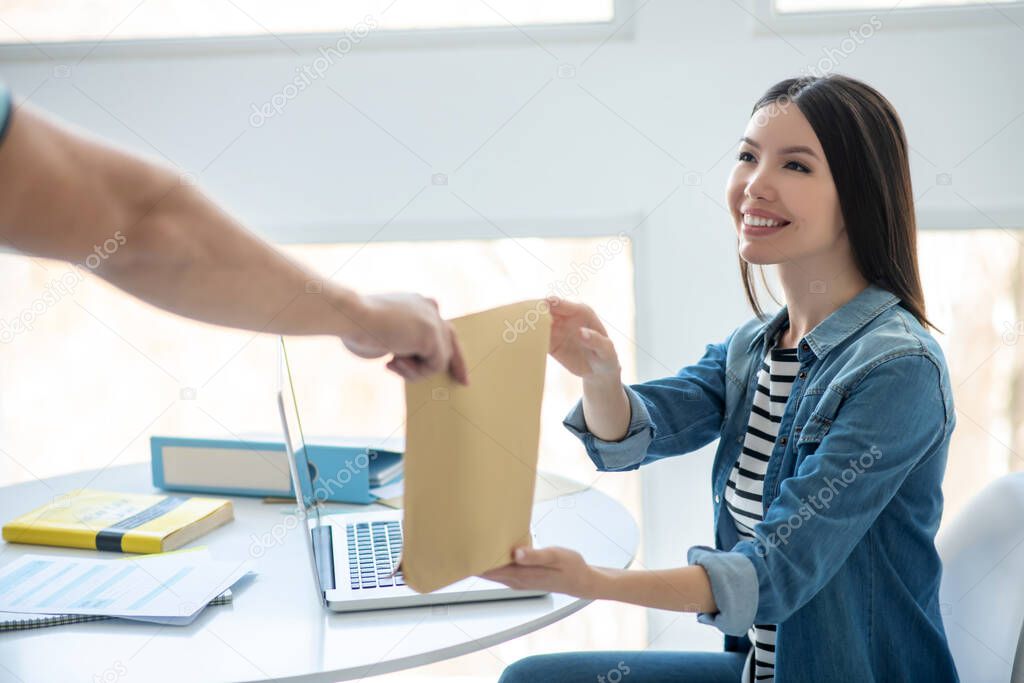 Smiling dark-haired female taking envelope from male hands