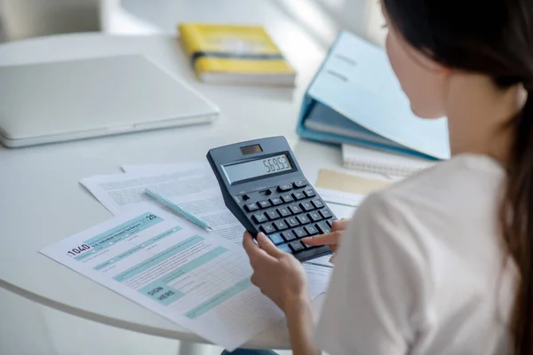Brunetka kobieta siedzi przy biurku, trzymając kalkulator — Zdjęcie stockowe
