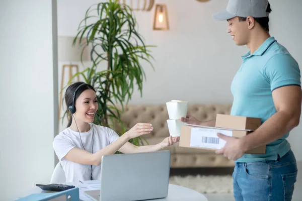 Dark-haired female receiving food boxes from brunette male courier, holding parcels