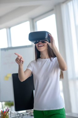 Koyu renk saçlı kız VR kulaklık takıyor ve eğleniyor.