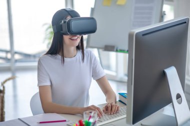 Koyu saçlı kız bilgisayarın başında VR kulaklık takıyor.