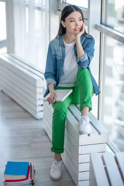 Young woman in a jeans jacket sitting near the window and thinking — Stock Photo, Image