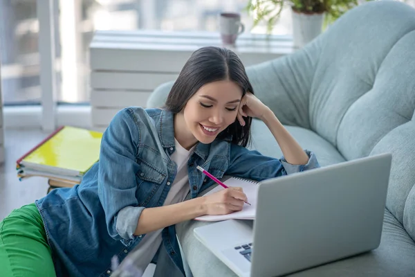 Mujer joven en una chaqueta vaquera sonriendo y estudiando remotamente — Foto de Stock