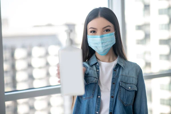 Dunkelhaarige Frau in Gesichtsmaske mit einer Flasche mit desinfizierender Flüssigkeit — Stockfoto