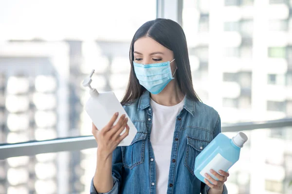 Femme aux cheveux bruns dans un masque facial choisissant un liquide désinfectant — Photo