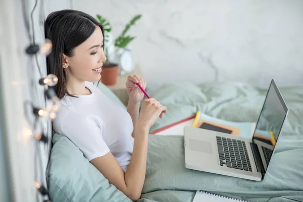 Giovane donna sorridente sdraiata sul letto e navigare su internet — Foto Stock