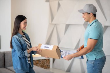 Esmer kadın, esmer erkek kuryeden paket alıyor.