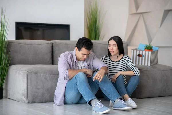 Unhappy young guy and long-haired wife are sitting on floor. — Stock Photo, Image