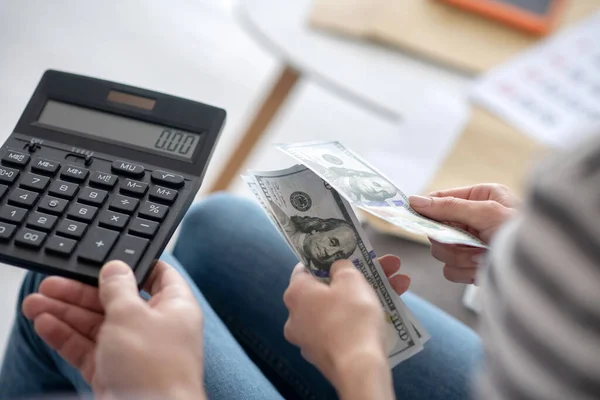 Mężczyzna trzyma kalkulator, kobieta ręce z banknotami dolarowymi. — Zdjęcie stockowe