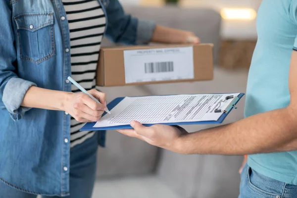 Manos femeninas sosteniendo el paquete y firmando los documentos de entrega — Foto de Stock