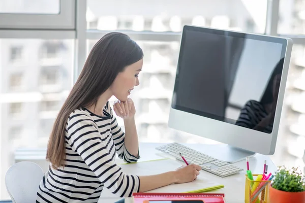 Donkerharige mooie vrouw in een gestreept shirt schrijft iets — Stockfoto