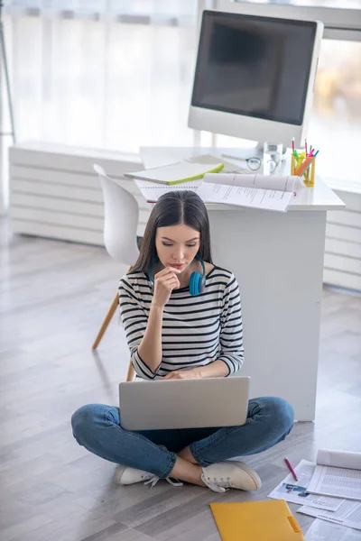 Menina de cabelos escuros com fones de ouvido trabalhando em um laptop e olhando confuso — Fotografia de Stock