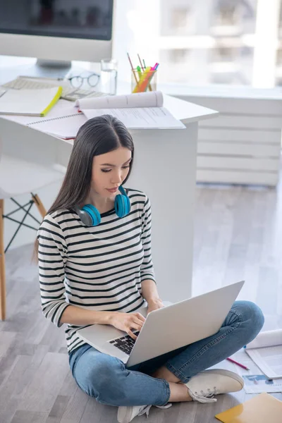 Ragazza dai capelli scuri con gli auricolari che lavorano su un computer portatile e sembrano sorpresi — Foto Stock