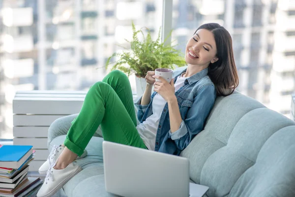 Mujer joven en una chaqueta vaquera sentada en el sofá y sintiéndose bien — Foto de Stock