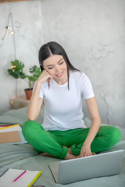 Giovane donna dai capelli scuri che fa una videochiamata mentre è seduta su un letto — Foto Stock