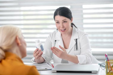 Elinde ilaç olan beyaz önlüklü bir kadın..