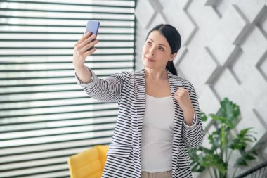 Güzel, yetişkin bir esmer, akıllı telefondan selfie çekiyor..