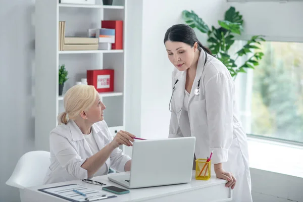 Två kvinnliga läkare i vita morgonrockar har en diskussion om fallet — Stockfoto