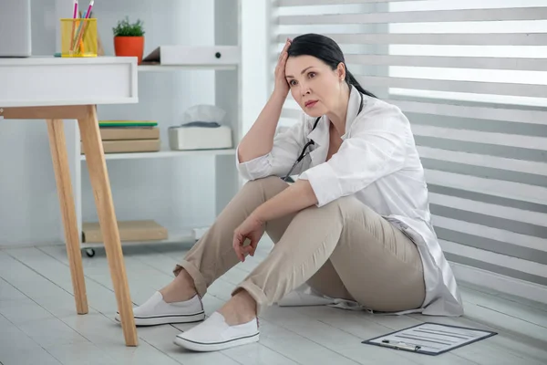 Žena doktor v bílém plášti sedí na podlaze. — Stock fotografie