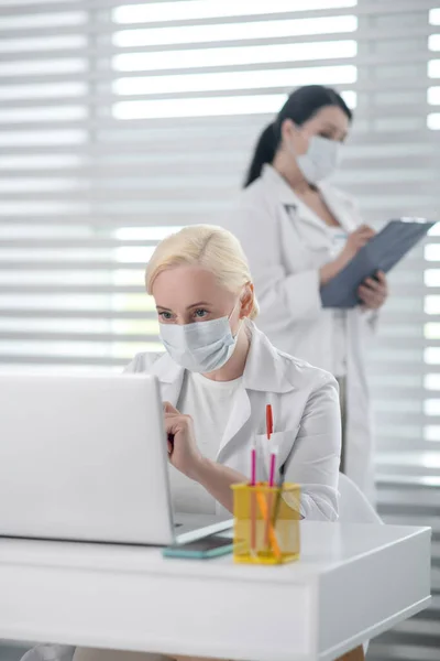 Dos mujeres con máscaras y batas blancas trabajando . — Foto de Stock