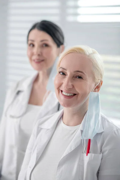 Two women in white coats with masks standing near window. — Stock Photo, Image