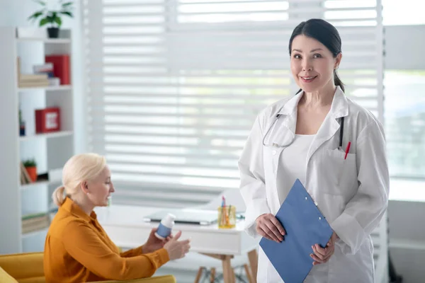 Vrouw in witte jas met map en patiënt met medicijnen. — Stockfoto