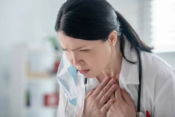 Volwassen donkerharige vrouwelijke arts in wit gewaad voelt zich slecht — Stockfoto