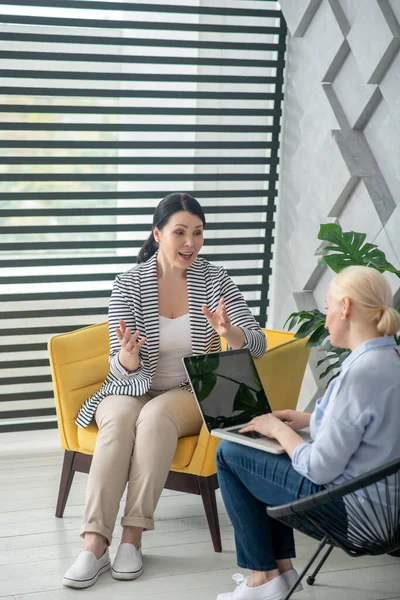 Mujer morena gesticulando rubia en un portátil . — Foto de Stock