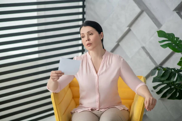 Beautiful sad woman in a light pink blouse in an armchair.