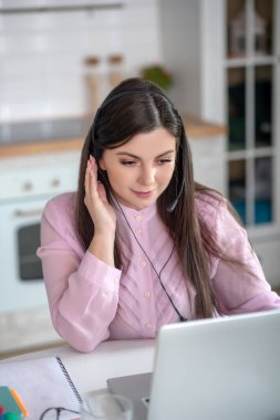 Pembe bluzlu genç bir kadın arıyor ve özenli görünüyor.