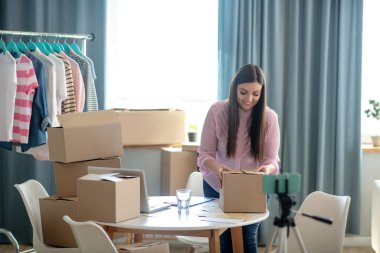 Koyu saçlı genç bir kadın bağış için kıyafetlerle kutuları paketliyor.