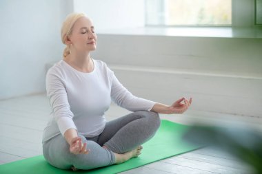 Nilüfer çiçeği pozunda oturmuş meditasyon yapan olgun sarışın kadın.