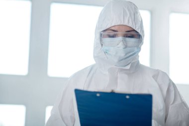 Koruyucu giysiler, tıbbi maske ve gözlük takan bir tıp çalışanı, klasöre bakıyor.