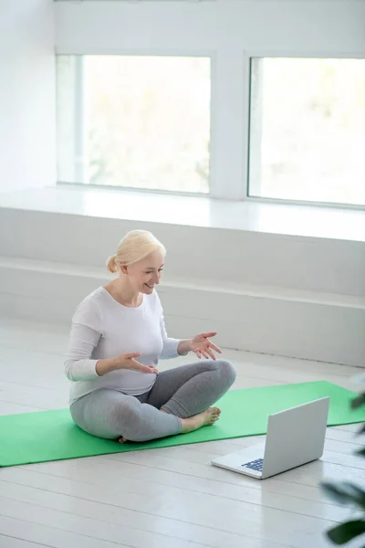 Nilüfer çiçekli poz veren olgun sarışın kadın internetten yoga dersi alıyor. — Stok fotoğraf