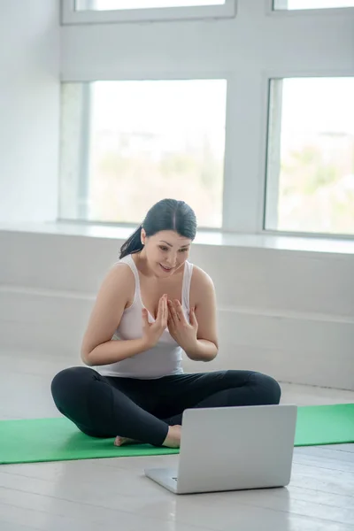Morena mujer sentada en la alfombra, hablando, teniendo clases de yoga en línea — Foto de Stock