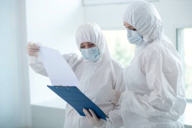 Koruyucu giysiler ve tıbbi maskeler içinde tıp çalışanları klasördeki kağıtlara bakıyorlar.