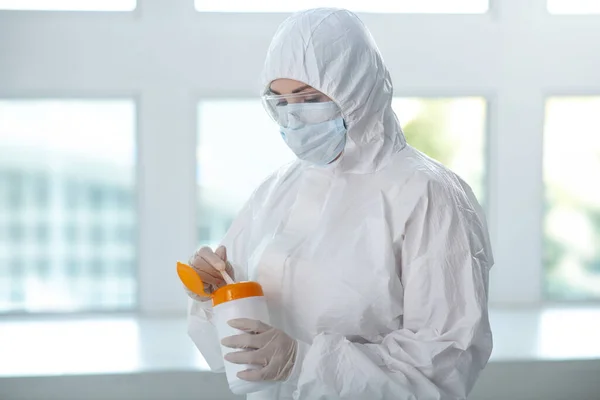 Медичний працівник в захисному одязі, медична маска та окуляри тримають пляшку для дезінфекції серветок, витягуючи одну — стокове фото