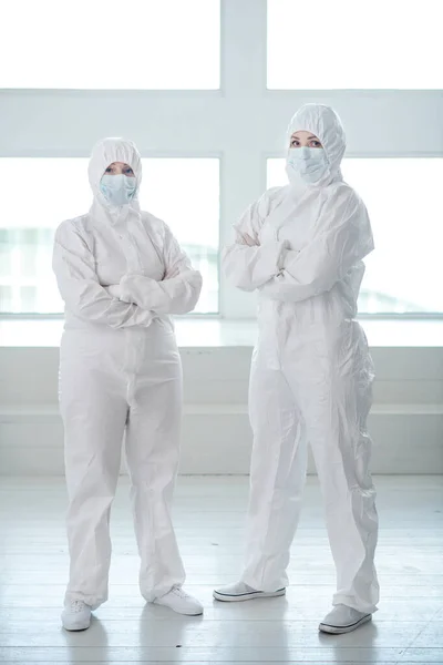 Trabajadores médicos con ropa protectora y máscaras médicas de pie con los brazos cruzados — Foto de Stock