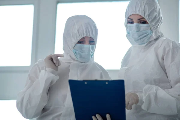 Медичні працівники в захисному одязі та медичних масках читають щось на кліпі — стокове фото