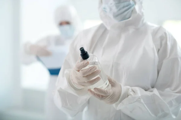 Κοντινό πλάνο του ιατρικού εργάτη χέρια κρατώντας αντισηπτικό μπουκάλι, ο συνάδελφός της στέκεται πίσω με το φάκελο κλιπ — Φωτογραφία Αρχείου