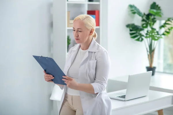 Блондинка середнього віку лікар тримає документи і читає — стокове фото