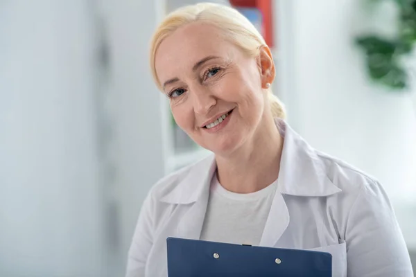 Médico de meia-idade loira sorrindo e olhando positivamente — Fotografia de Stock