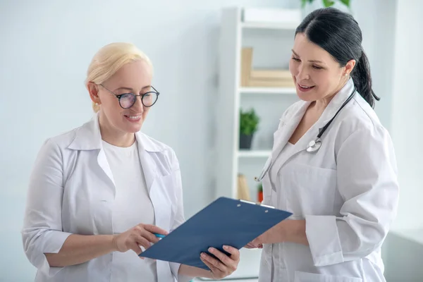 Twee vrouwelijke artsen die de medische geschiedenis lezen en er positief uitzien — Stockfoto