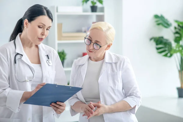 Två kvinnliga läkare läser sjukdomshistoria och ser allvarliga — Stockfoto